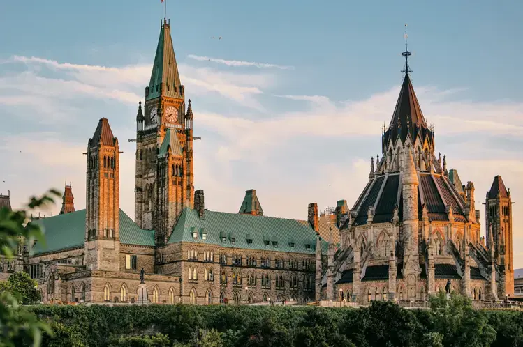 メジャーズ ヒル パークから、緑と柔らかな青空に囲まれた夕日の光に輝く象徴的なゴシック様式の塔を眺めます。