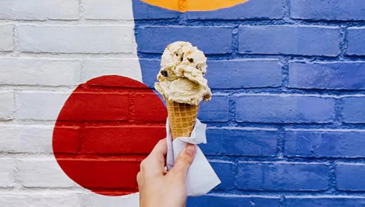 Close-up of a hand holding an ice cream cone in front of Flurple’s.