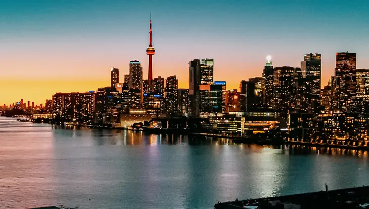 青とピンクの夕焼けの下、夜に輝く建物が並ぶトロントのスカイライン。