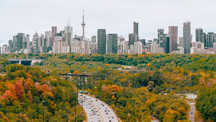 秋の紅葉の森に囲まれたトロントのスカイラインへと続く高速道路の街並みの眺め。