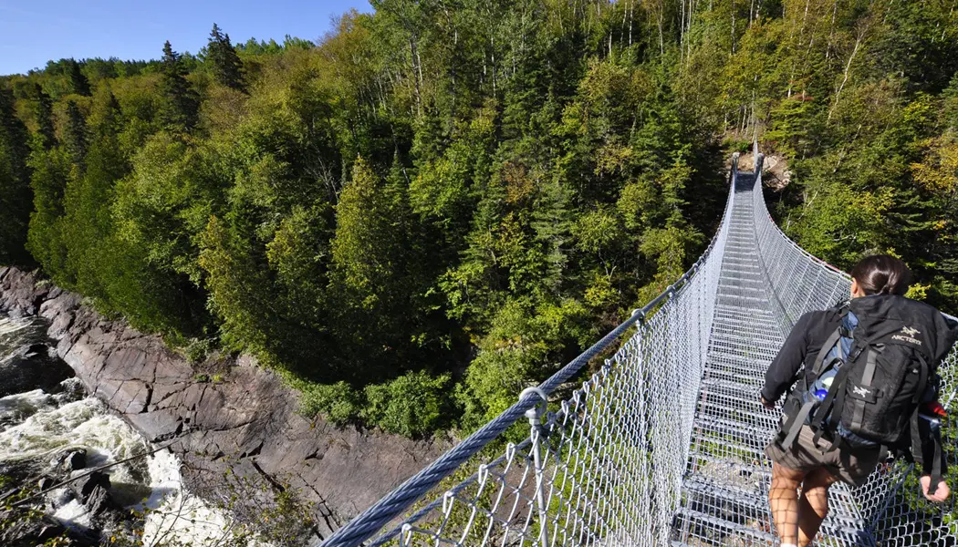Un excursionista cruzando el puente colgante del río Blanco en el Parque Nacional Pukaskwa.