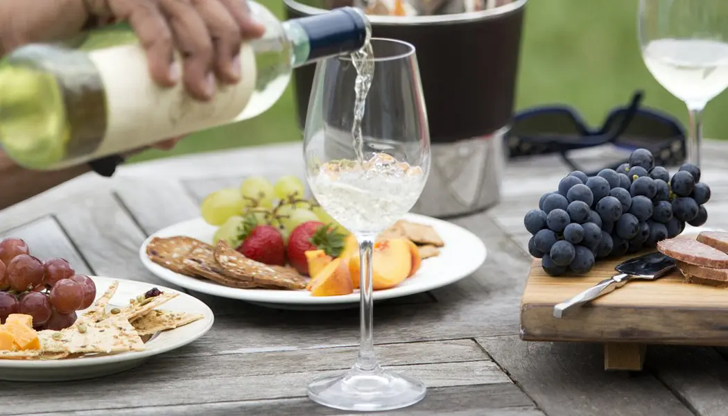 Eine Person schenkt sich ein Glas Weißwein ein, um ein Picknick im Freien mit Obst und Käse im Viewpoint Estate Winery zu begleiten.
