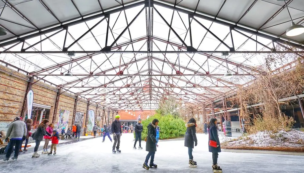 Plusieurs personnes s’amusent à patiner sur une patinoire en plein air sous les poutres d’une usine de briques à Evergreen Brickworks.