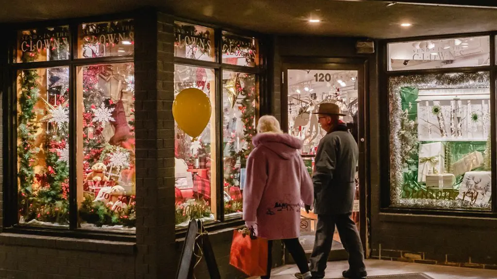 Una pareja pasa frente a los escaparates de una tienda iluminada por la noche y decorada para las fiestas.