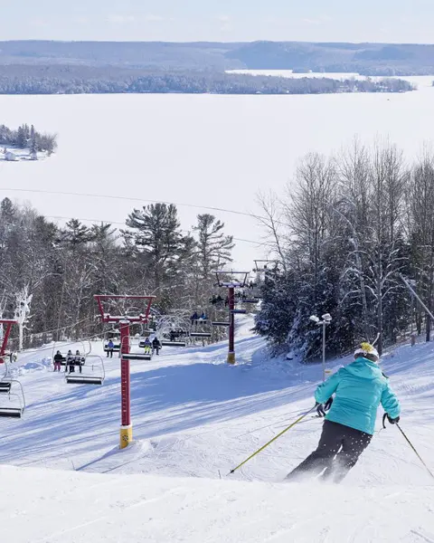 青い冬用コートを着たアルペンスキーヤーが、マスコーカのヒドゥンバレーにあるスキーコースを滑降している。
