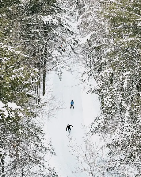 Vista aérea de dos personas patinando sobre hielo en una pista de patinaje bien mantenida a través del bosque en Arrowhead Park.