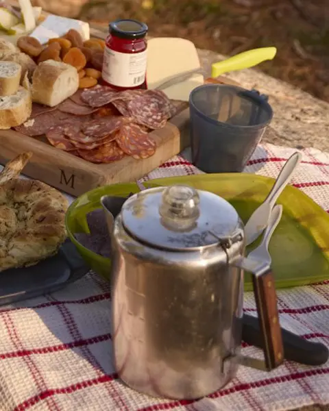 広大な湖を見下ろすキャンプ場で、カップルが燃え盛る火の前の丸太のベンチに座っている。