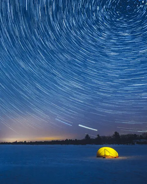 Ein gelbes Zelt in der verschneiten Nachtlandschaft der Torrance Barrens in Muskoka wird vom hellen Licht des Sternenhimmels erleuchtet.