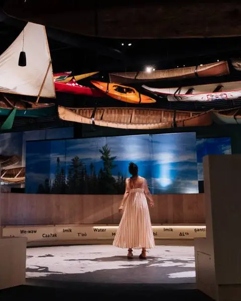 A woman explores a gallery of watercraft, including heritage canoes and kayaks, on a behind-the-scenes tour at the Canadian Canoe Museum.