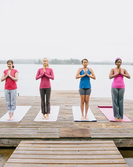 Group of people meditating on a wooden dock overlooking a calm lake.