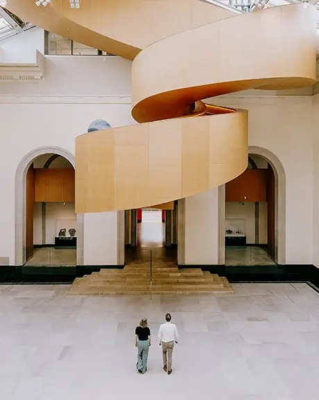 Spacious museum atrium with curved balconies and visitors walking across an open floor.