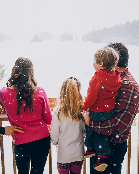 다섯 명으로 이루어진 가족이 눈 덮인 발코니에 서서 눈 덮인 숲 풍경을 바라보고 있다.