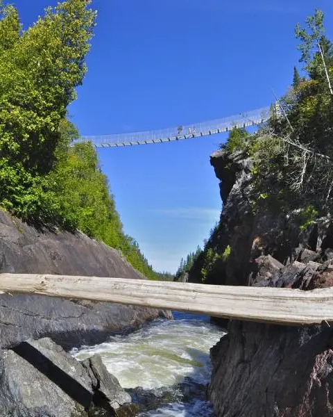 Unos excursionistas cruzan un puente colgante peatonal situado a gran altura sobre las aguas turbulentas a lo largo de una ruta de senderismo en el Parque Nacional de Pukaskwa.