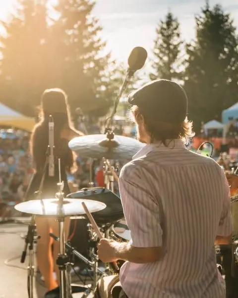 Vue par-dessus l'épaule d'un batteur d'un groupe se produisant sur scène lors d'un festival de musique en plein air.