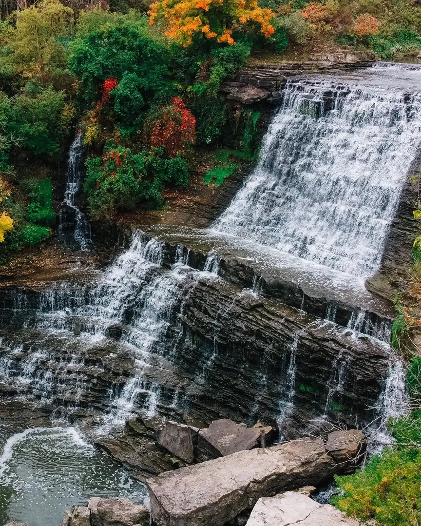 Cascada que cae en cascada rodeada de árboles con los colores del otoño.