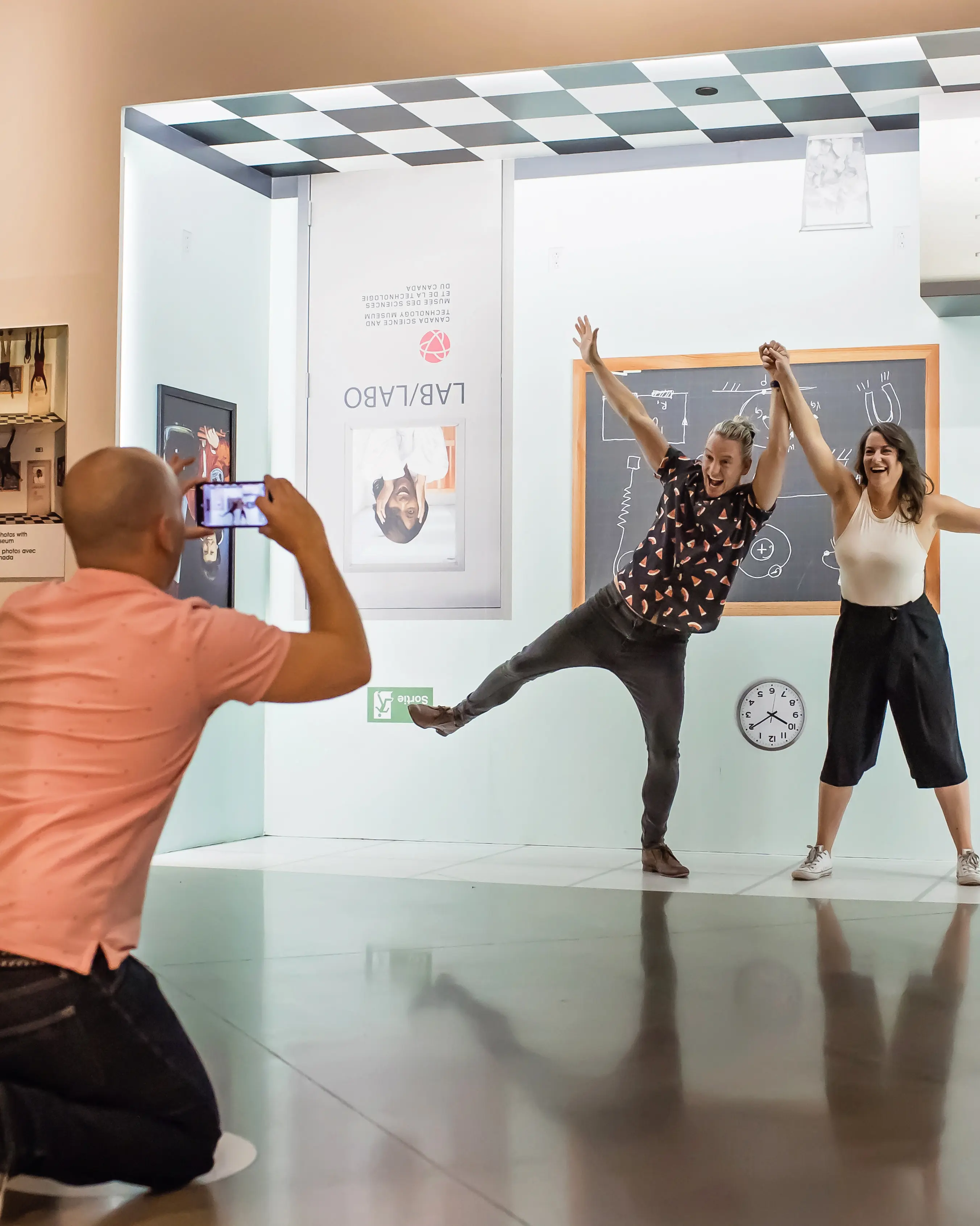 Zwei Besucher posieren spielerisch in einer Laborausstellung im Kanadischen Wissenschafts- und Technologiemuseum, während eine dritte Person sie fotografiert.