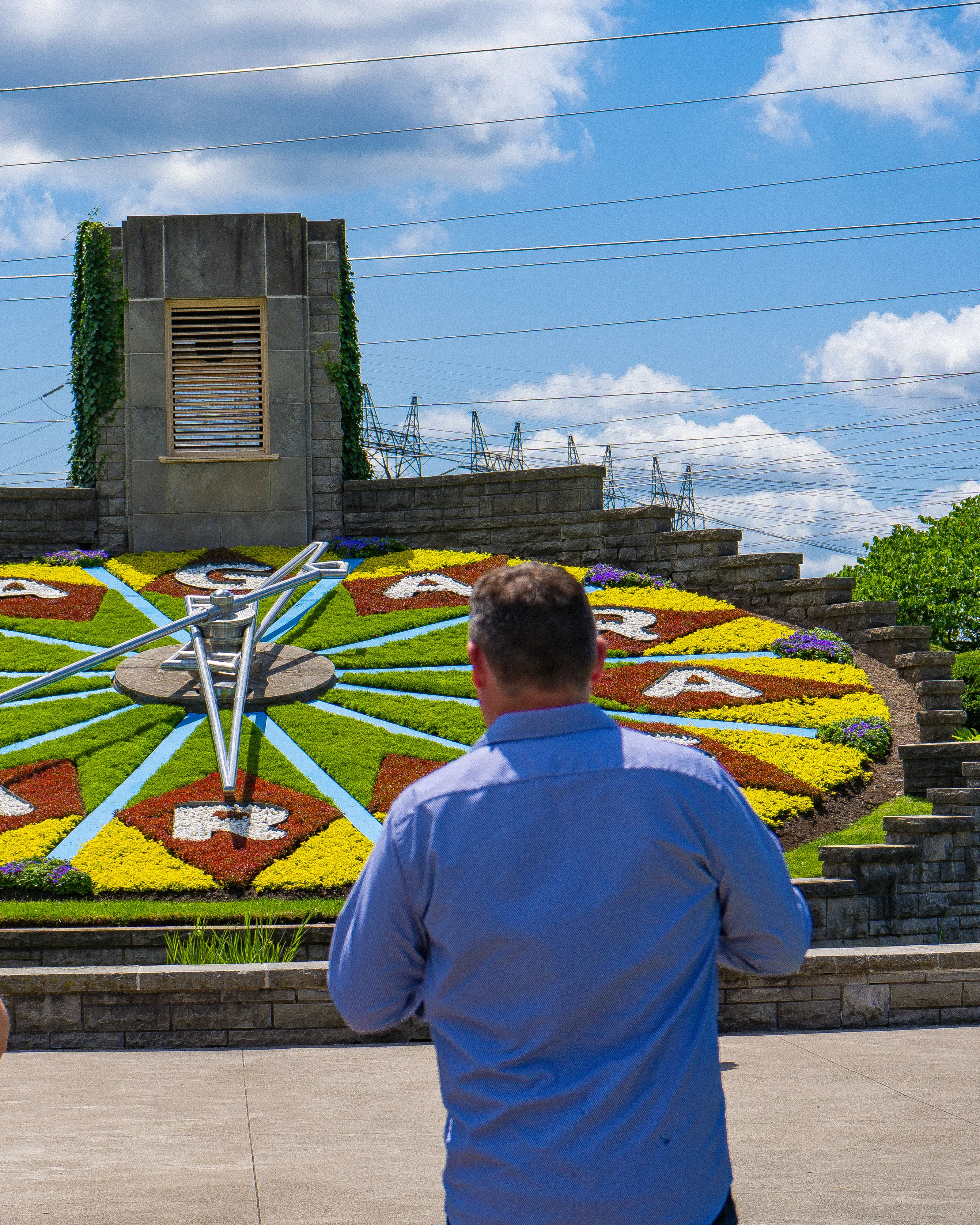 Three visitors viewing the Niagara Floral Clock, a large working clock face made of colorful flowers spelling 'Niagara Falls.