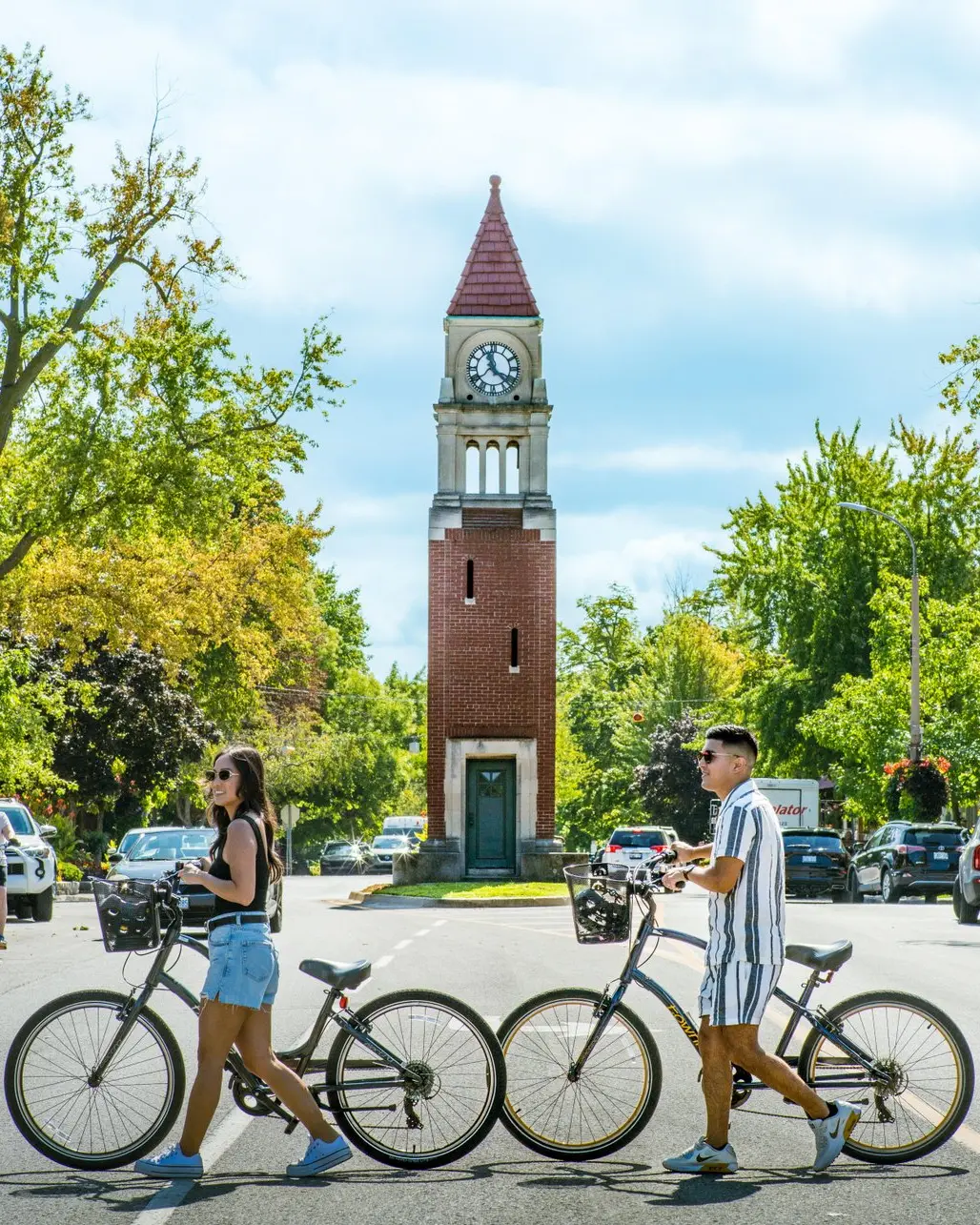 Four people with bicycles crossing the street in front of the clock tower.
