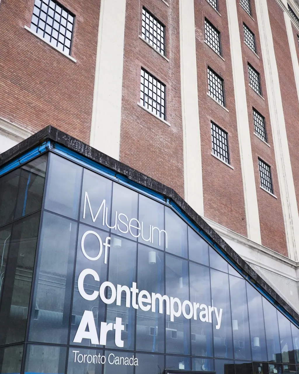 The glass entrance of the Museum of Contemporary Art Toronto, set against the historic red brick Tower Automotive Building.