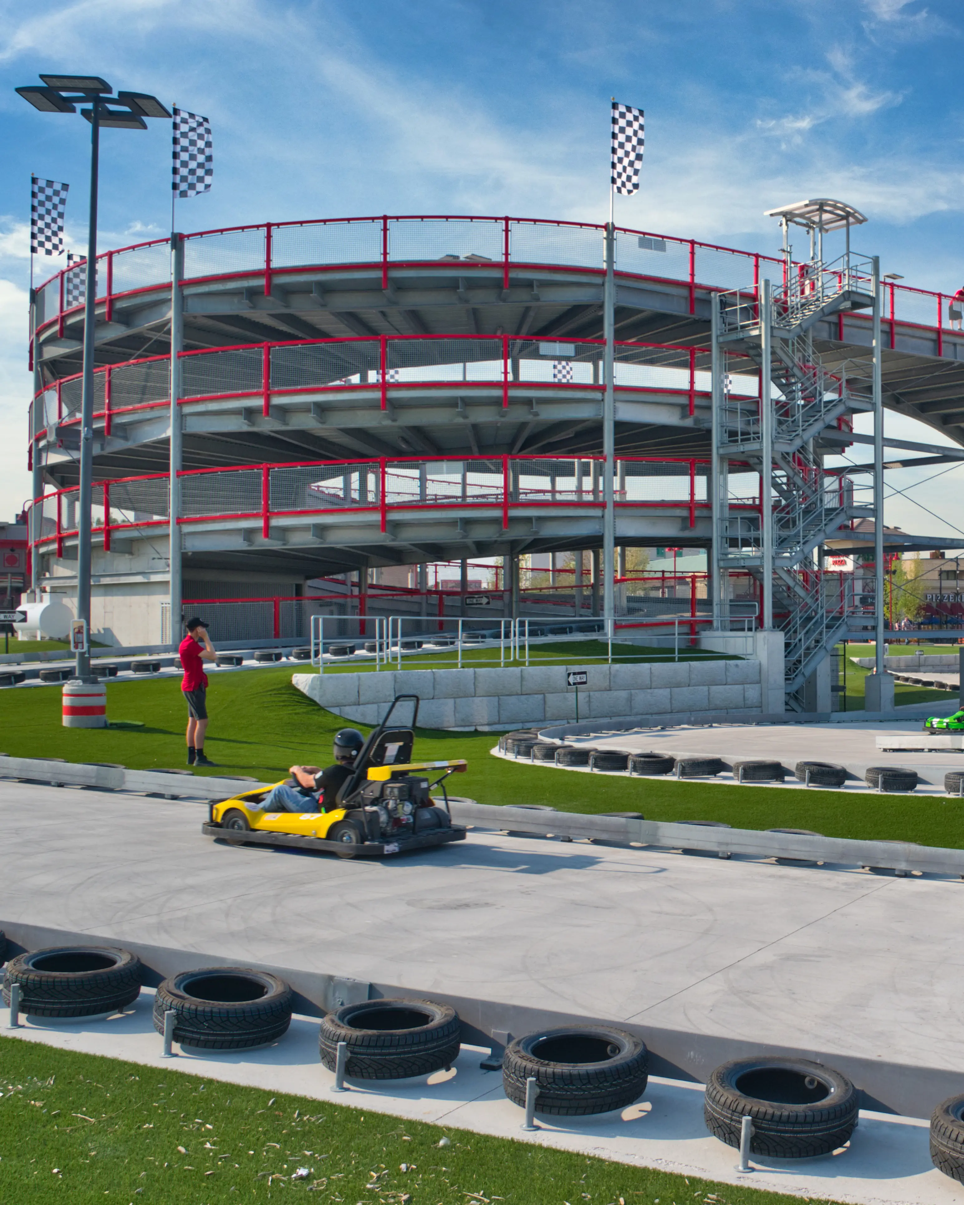 Multi-level go-kart track with a spiral ramp structure, checkered flags, and colorful karts racing on a concrete course.