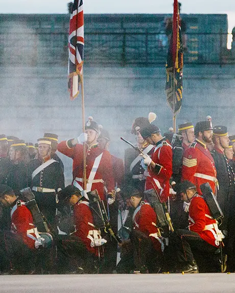 Garde du Fort Henry en uniforme rouge historique, entourée de fumée, effectuant un exercice cérémoniel à Kingston au crépuscule.