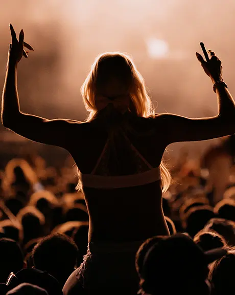 Personne sur les épaules d’une autre parmi une foule à un festival de musique en plein air en soirée.