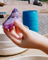 Someone holding a puple and blue amethyst at the beach. 