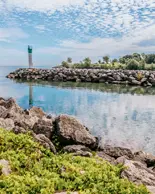 Partially cloudy sky is reflected on the body of water with large rocks where the water meets the grass.