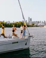 Groupe de personnes en train de socialiser sur un voilier naviguant sur l’eau, avec le centre-ville de Toronto et la Tour CN en arrière-plan.