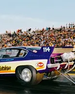 A large crowd of fans watch cars race at the Grand Bend Motorplex.