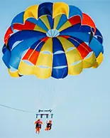 Two people gliding with a red, blue and yellow parasail in the clear sky.
