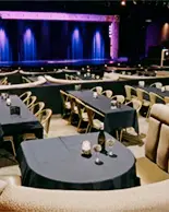 Banquettes incurvées et tables rondes faisant face à une scène éclairée dans une élégante salle de théâtre.
