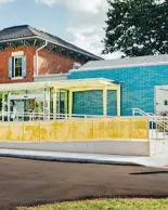 Zwei Kinder rennen auf dem Bürgersteig weg von den braunen und blauen Gebäuden des Hamilton Kindermuseums.