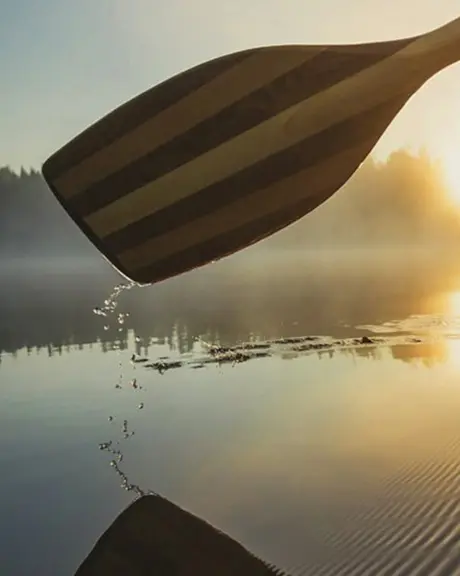 A canoe paddle gently rows through water off into a sunset.