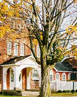 A large tree with yellow and orange leaves partially blocks the view of the Niagara-on-the-Lake Museum.