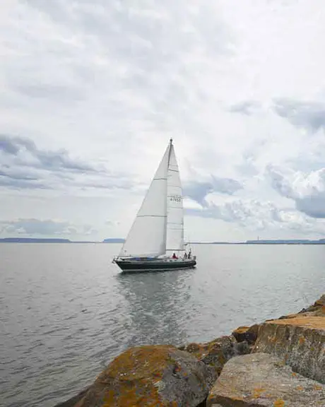 Un voilier passe devant un phare blanc et rouge au sommet d'une côte rocheuse