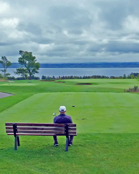 A man sits on a bench overlooking the greens of a golf course.