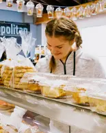 A person wearing a zip up sweater looking at a plethora of pastries and other baked goods at a bakery. 
