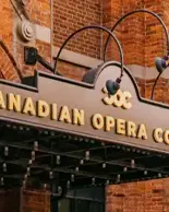 Sign reading “Canadian Opera Company” mounted on a brick building, with curved metal supports and lighting above the entrance.
