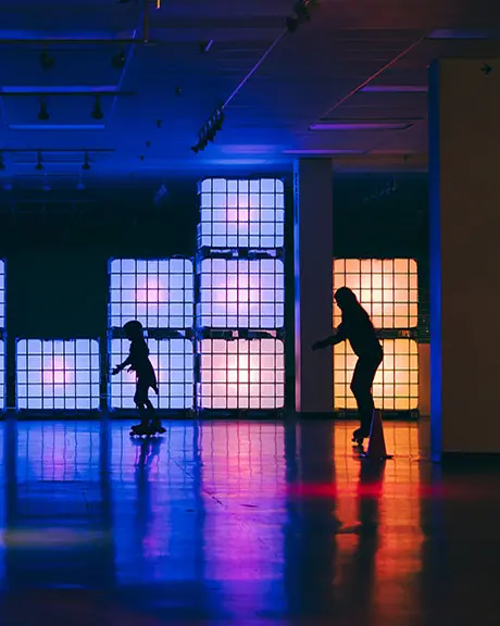 Three kids roller skating in front of colourful, glow up blocks.