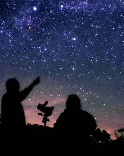 La silhouette de deux personnes qui regardent et pointent les étoiles.
