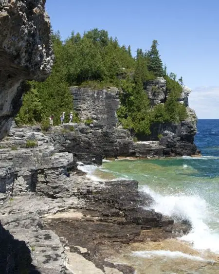 Three people hike along a rocky shoreline overlooking blue water of Georgian Bay.
