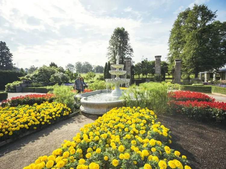 한 커플이 왕립 식물원의 화단으로 둘러싸인 화려한 분수 옆을 걷고 있습니다.