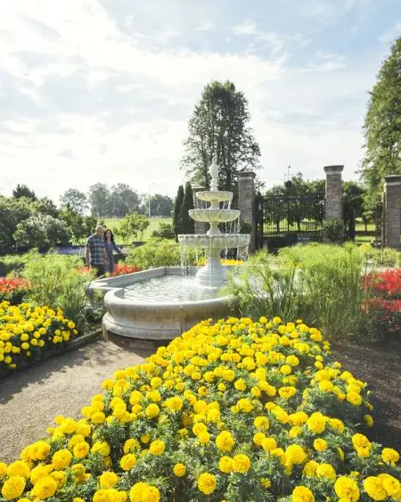 A couple walk past an ornate fountain surrounded by flower beds at Royal Botanical Gardens.
