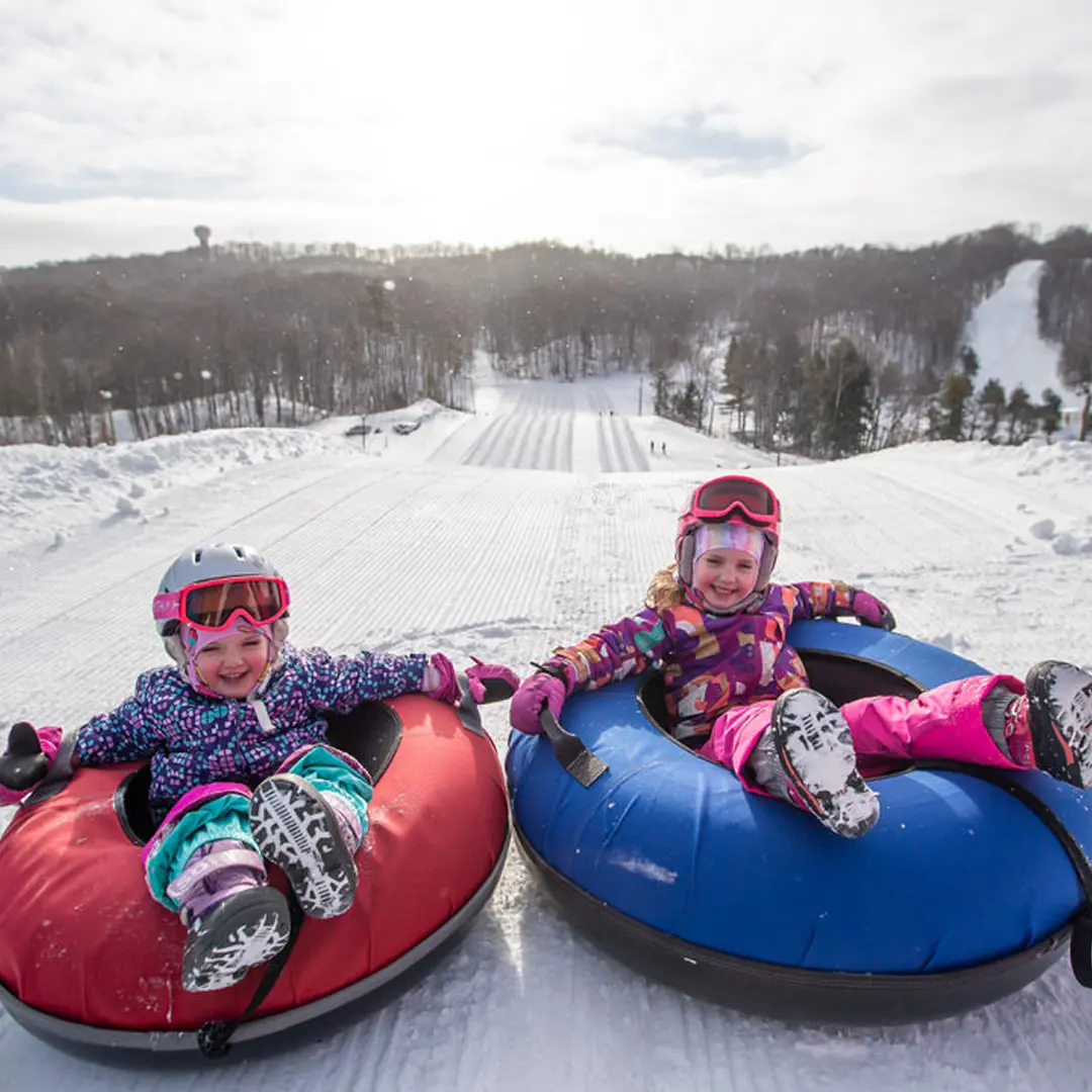 Deux enfants assises sur des chambres à air en haut d’une pente enneigée au centre de villégiature Horseshoe.