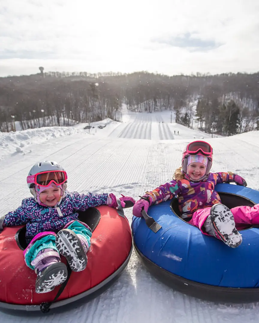 Two children sitting on snow tubes in front of a snowy hill at Horseshoe Resort.