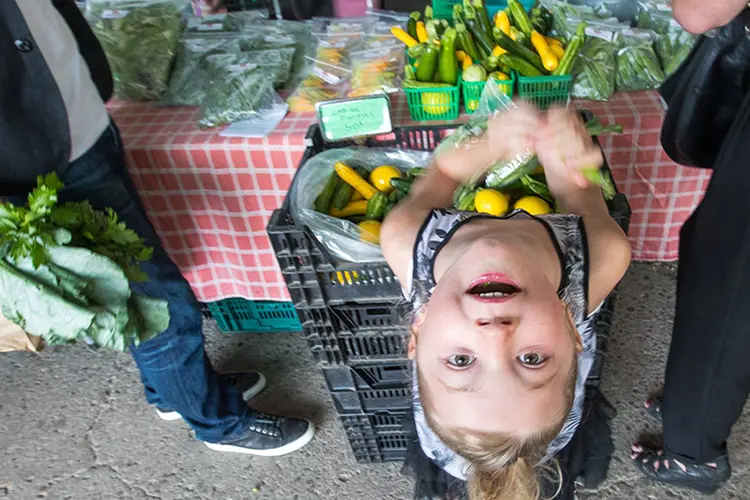 Ein junges Mädchen blickt von einem Verkaufstisch auf einem Bauernmarkt auf.