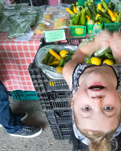 A young girl looks up from a vendors table at a farmers’ market.