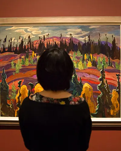 A woman stands in front of a Group of Seven painting.