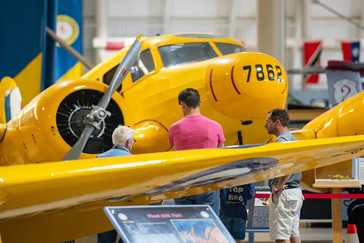 Three people view a vintage aircraft at an aviation museum.